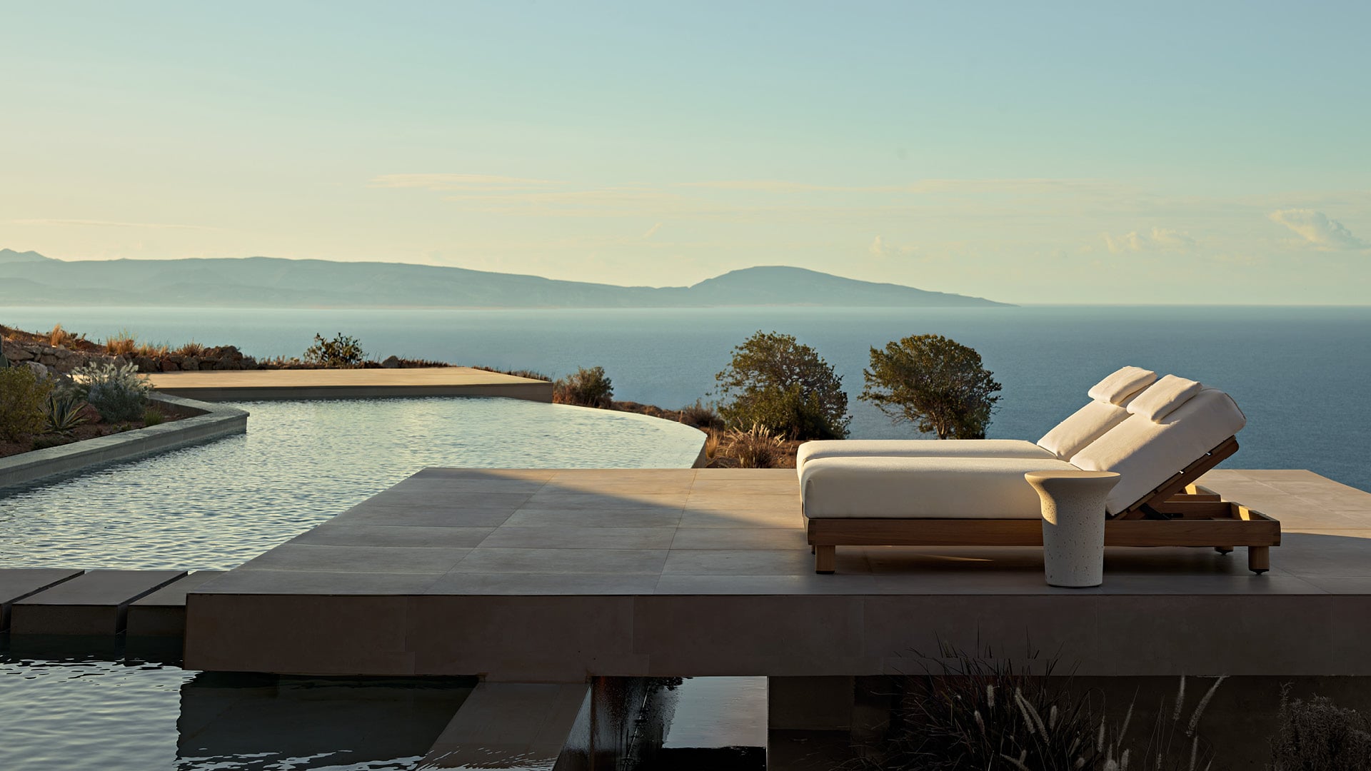 Ambiente exterior en una villa moderna, zona de piscina con tumbonas Ketch, mesa auxiliar Reef en Cementoraw® crema.