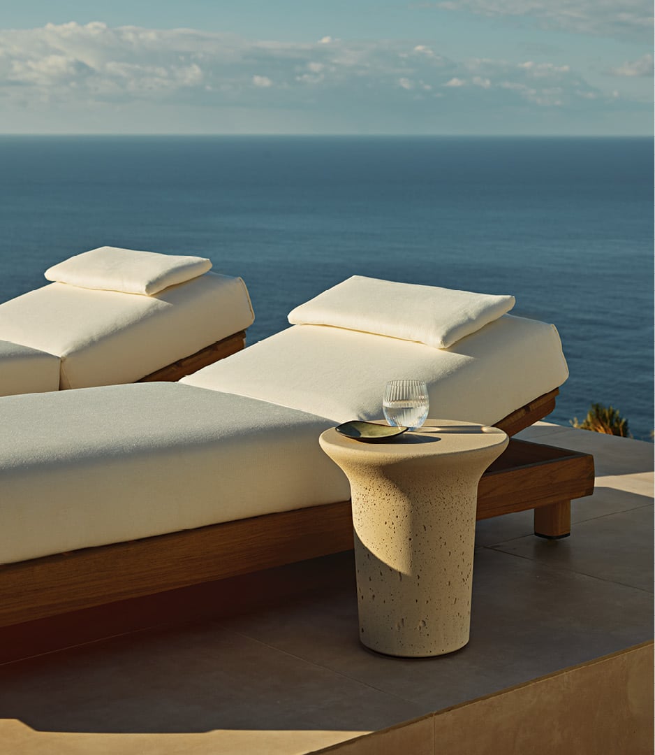 Ambiente exterior en una villa moderna, zona de piscina con tumbonas Ketch, mesa auxiliar Reef en Cementoraw® crema.